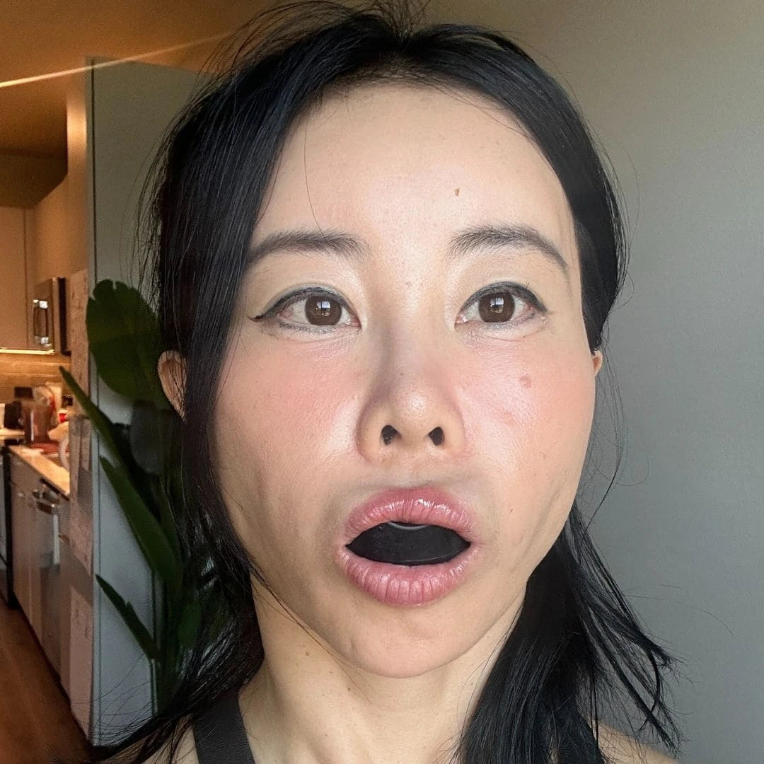 Woman holding Face Yoga aligner in mouth to activate facial muscles naturally.