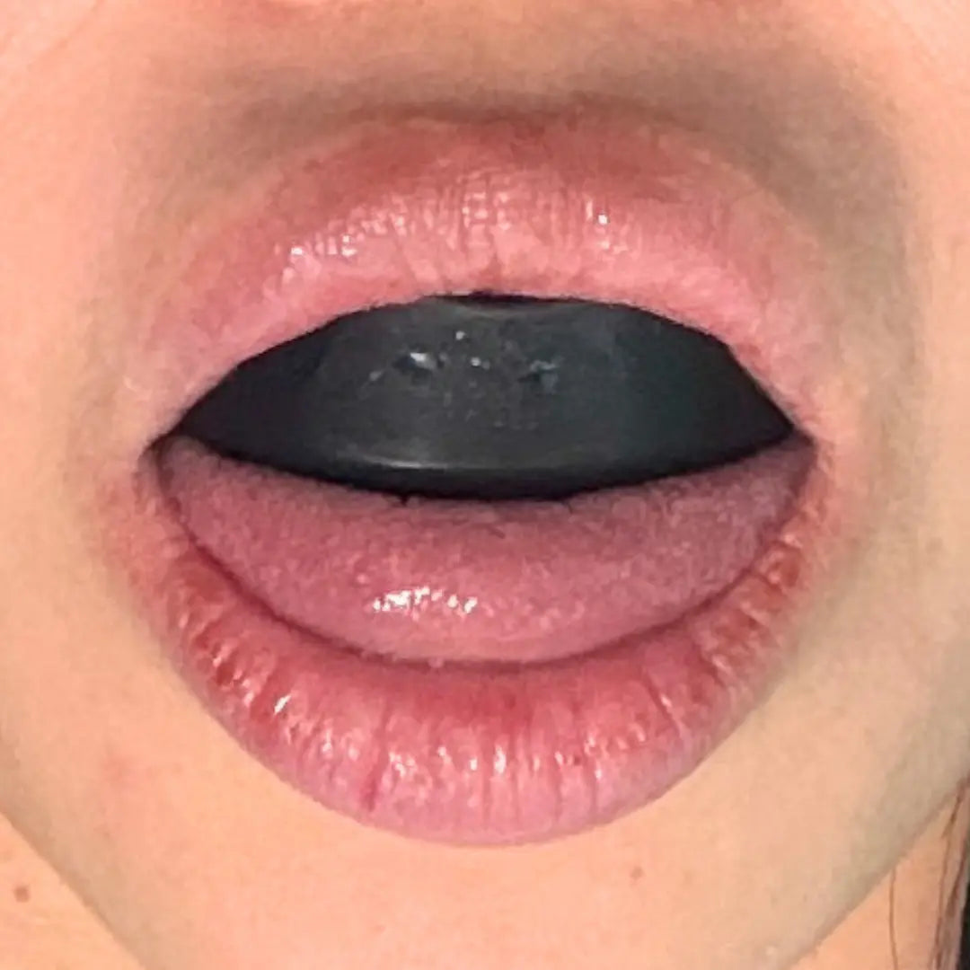 Close-up of mouth with black Essential facial aligner inserted, demonstrating Step 2 of Koko Face Yoga muscle activation exercise.